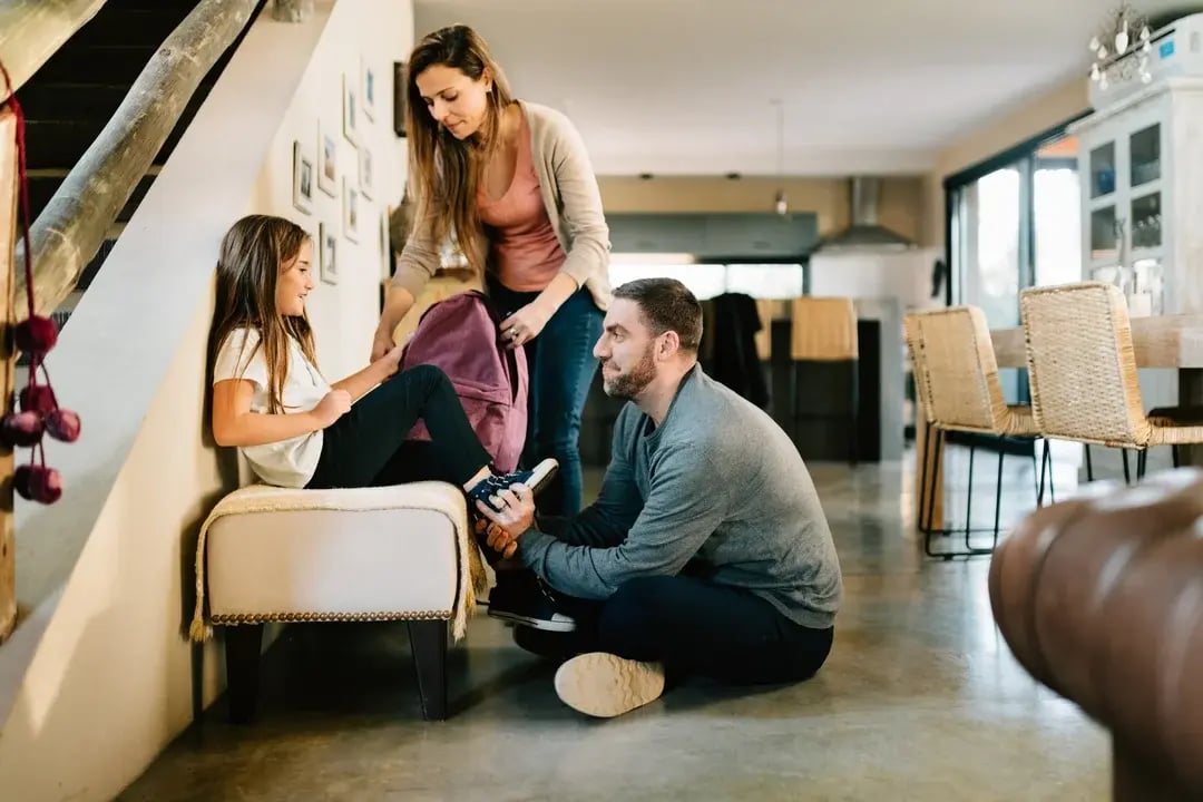 Parents et fille montant les escaliers dans une maison moderne, vue côté cuisine.
